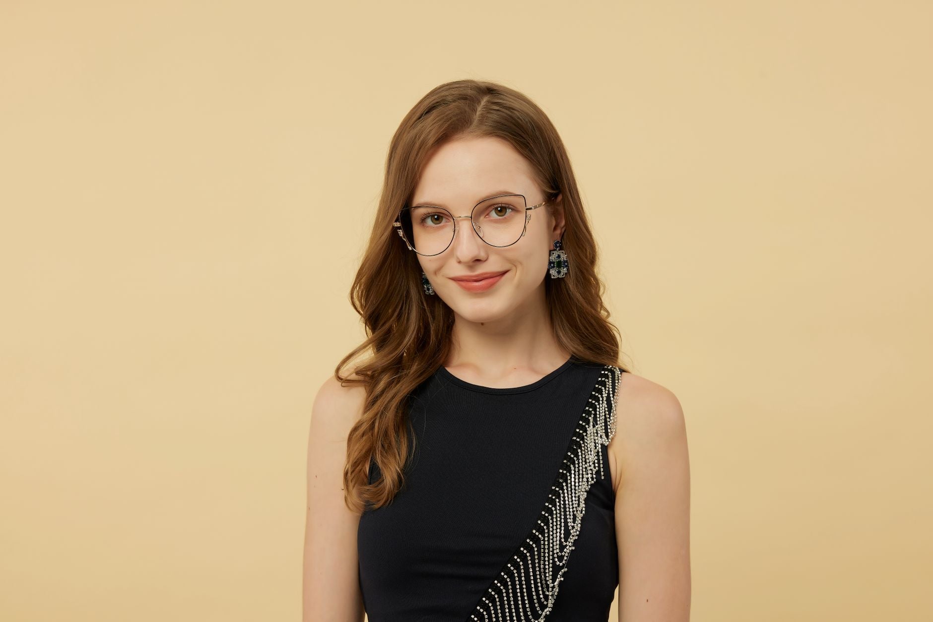 Portrait of a young woman wearing stylish eyeglasses and an elegant black dress with a beaded design, against a neutral background.