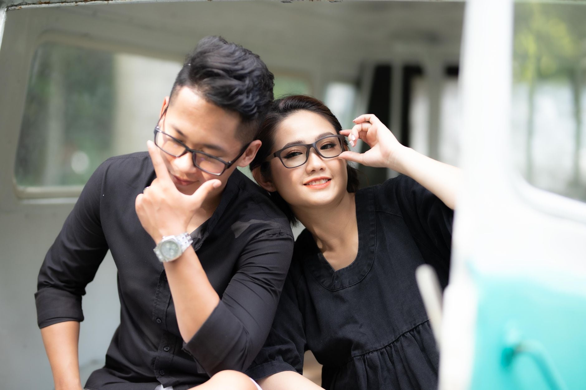 Asian couple in black clothes, posing playfully. Modern style with a bright backdrop.
