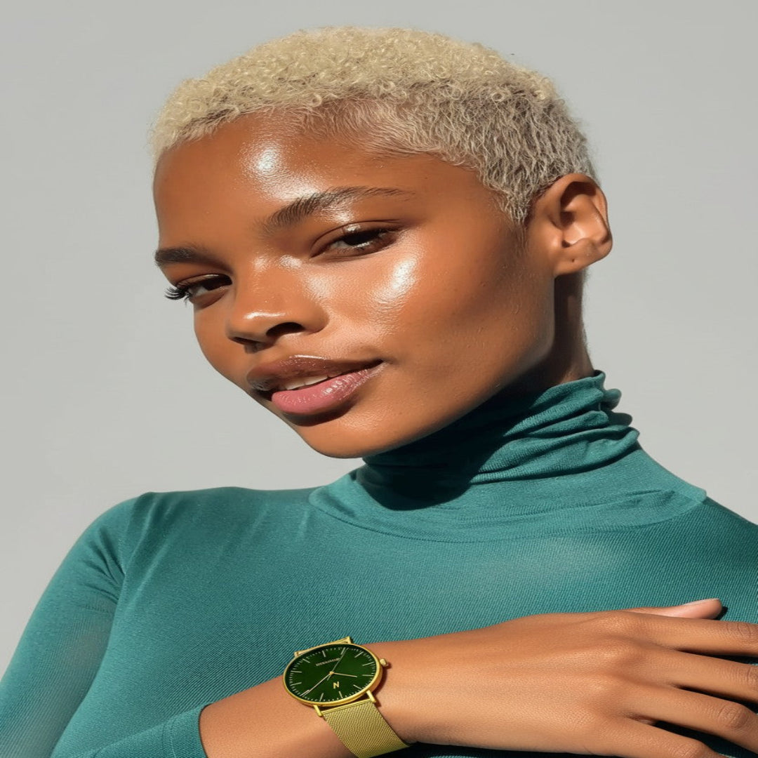 Woman wearing a teal turtleneck and yellow gold watch against a gray background