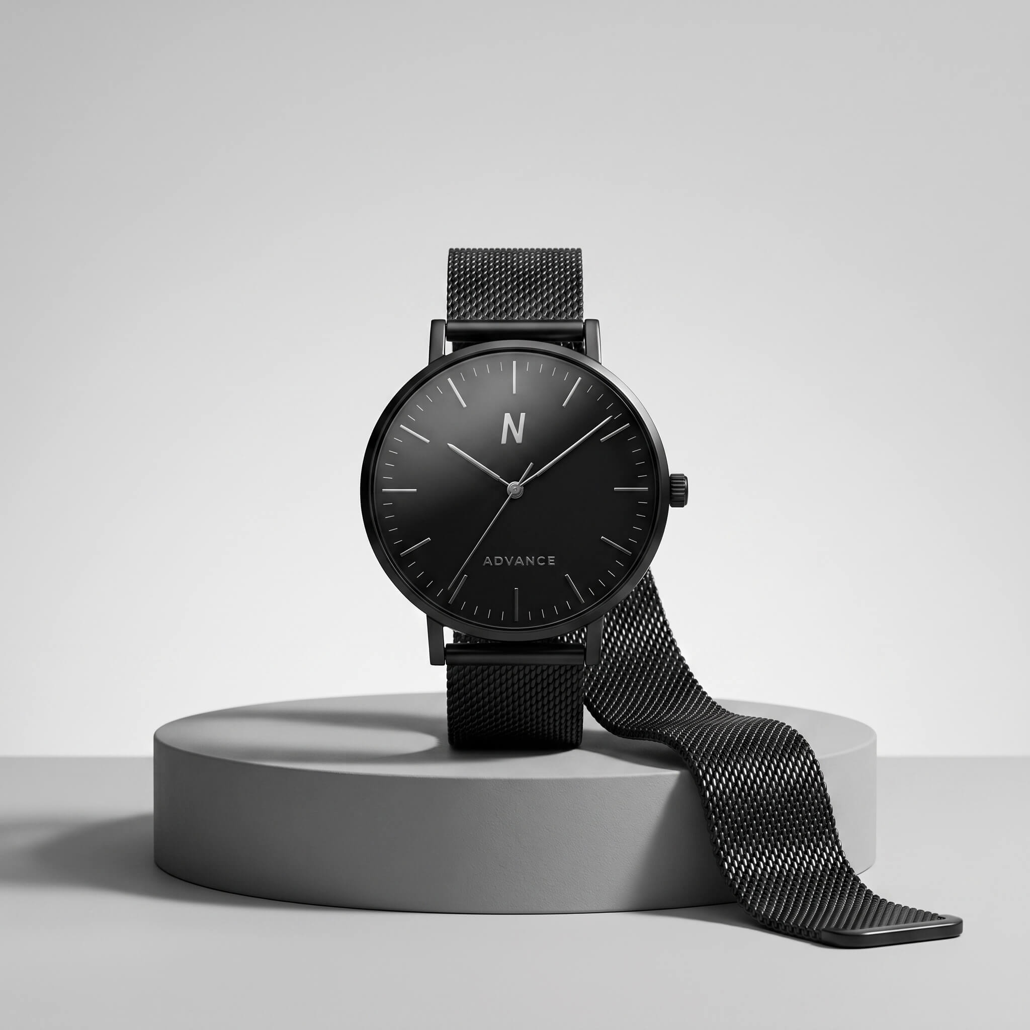 A minimalist black analog watch with a black dial, black mesh strap, and a visible 'N ADVANCE' logo on the face, displayed on a round gray pedestal against a light gray studio background.