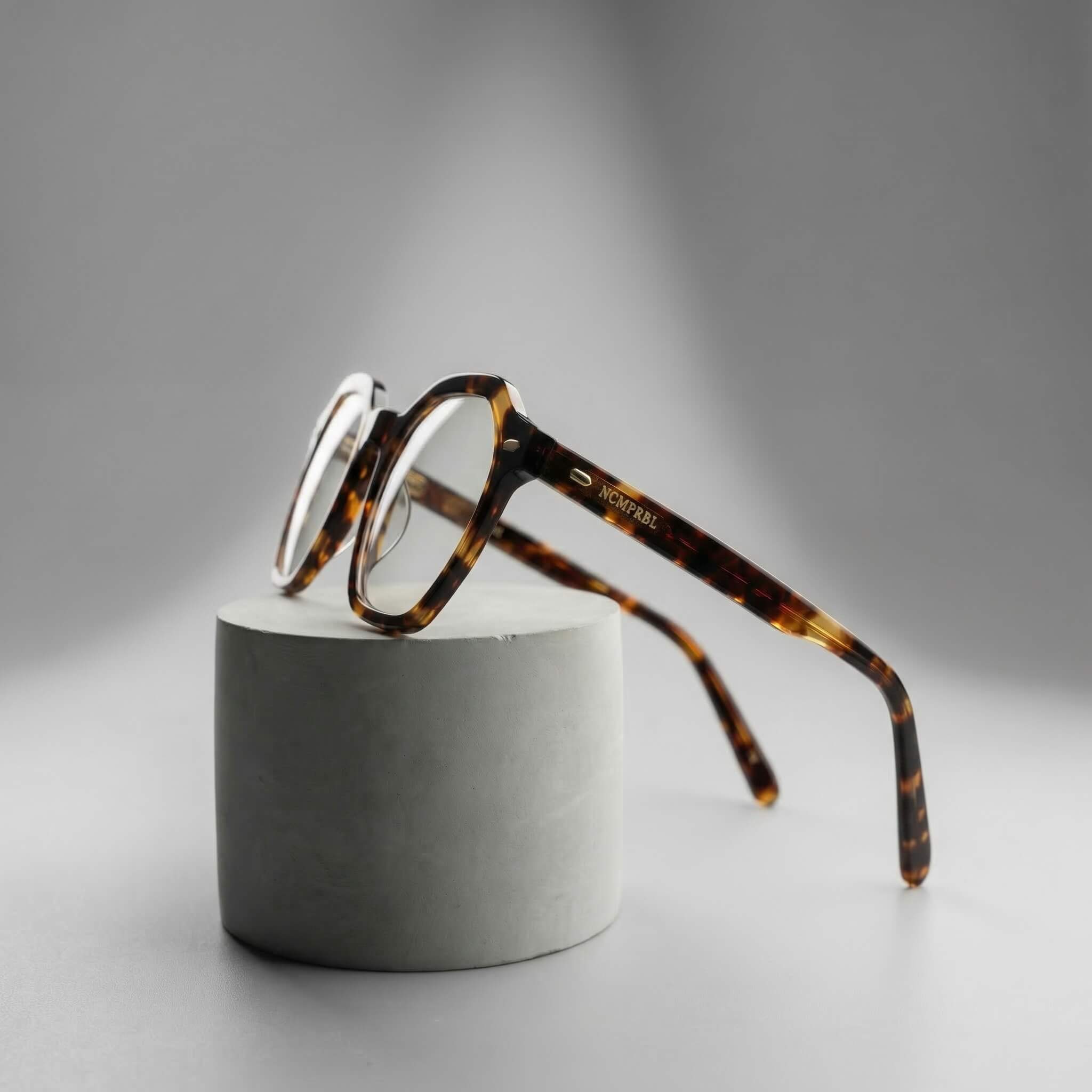 Tortoiseshell eyeglasses on a gray pedestal against a gray background
