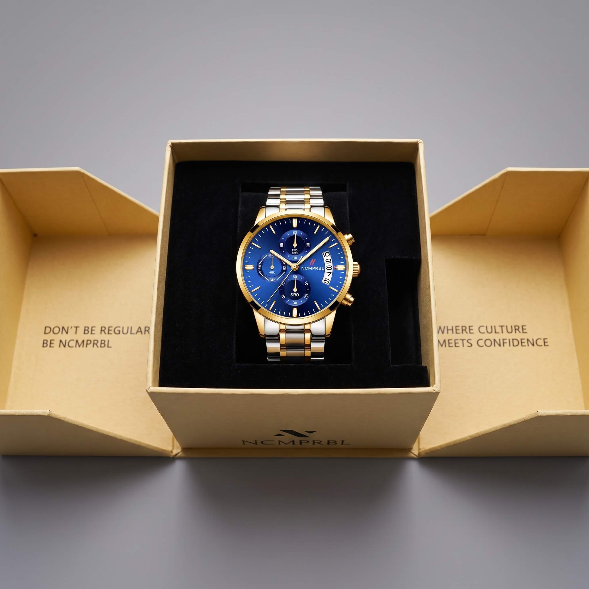 A luxury men's watch with a blue dial and gold-tone/silver-tone stainless steel case, presented inside an open gold-colored brand box on a neutral gray background.