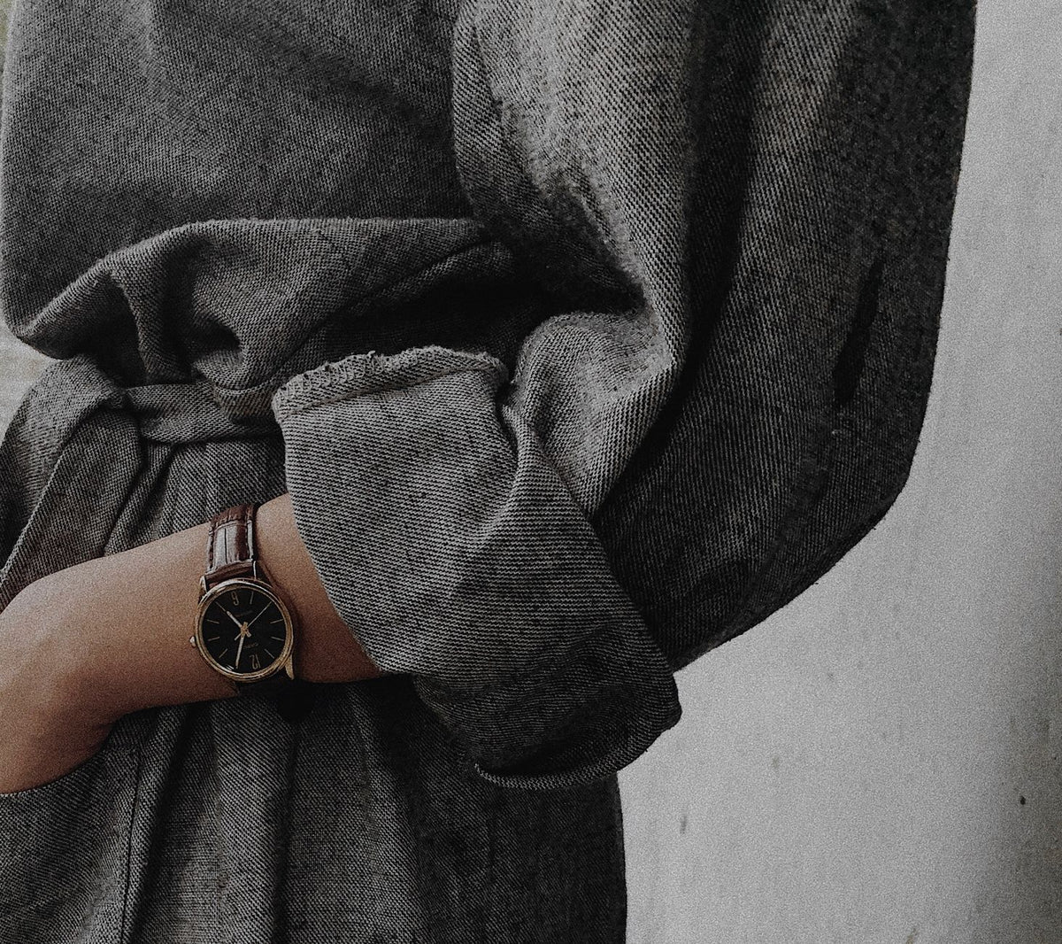 Close-up of a person's arm wearing a classic watch and a textured grey jacket, showcasing elegance.