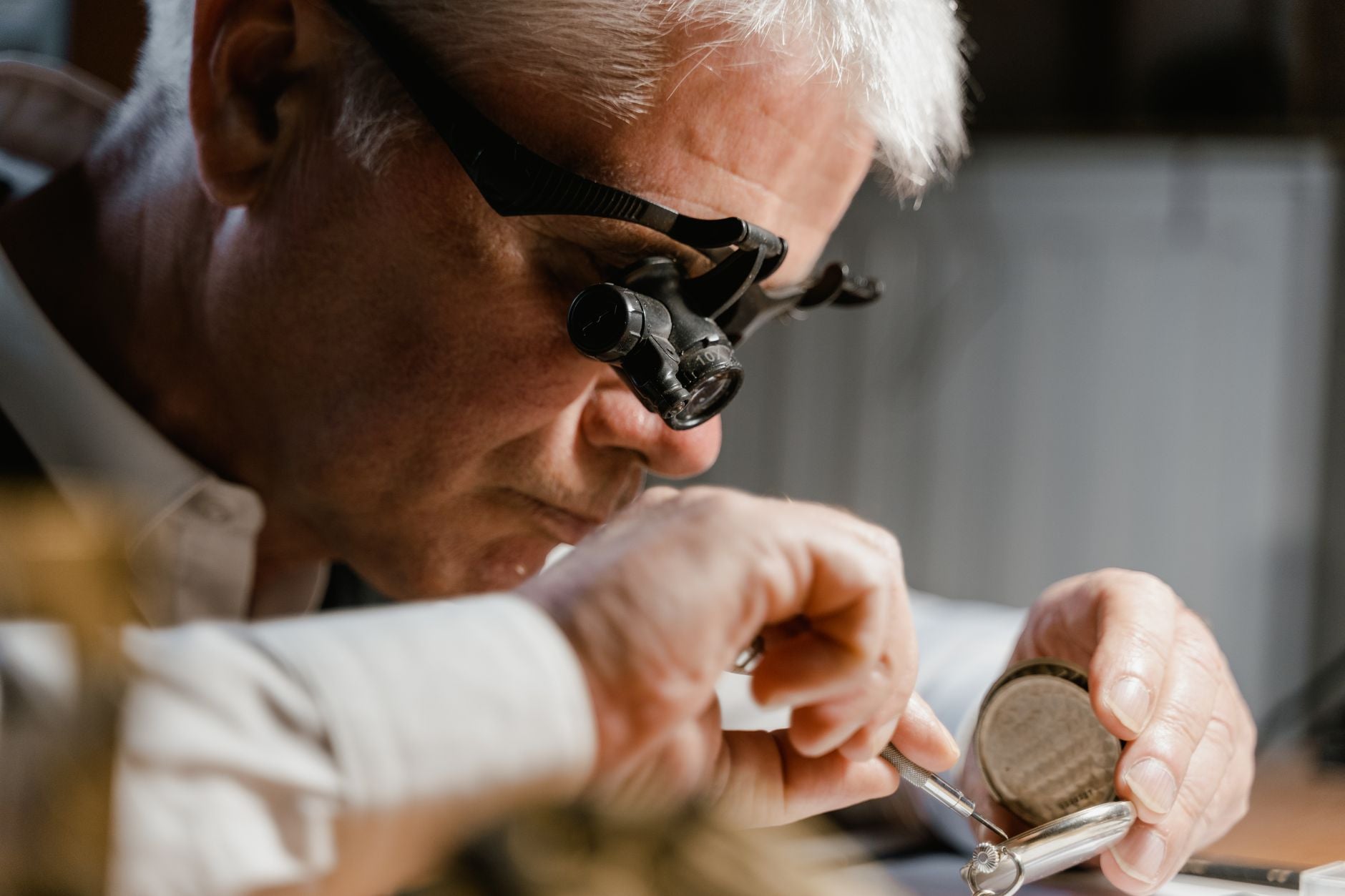 Watchmaker in action repairing a clock with precision tools in workshop setting.