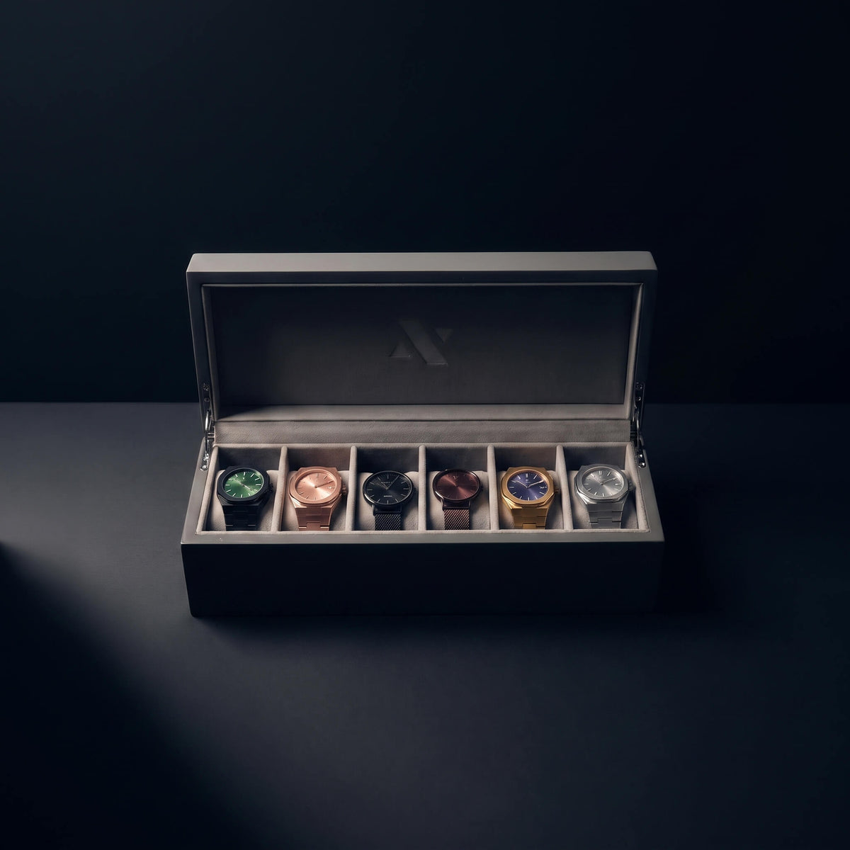A luxury watch display box with an open lid, showcasing six different wristwatches in individual slots. The watches feature various metal cases and dials.