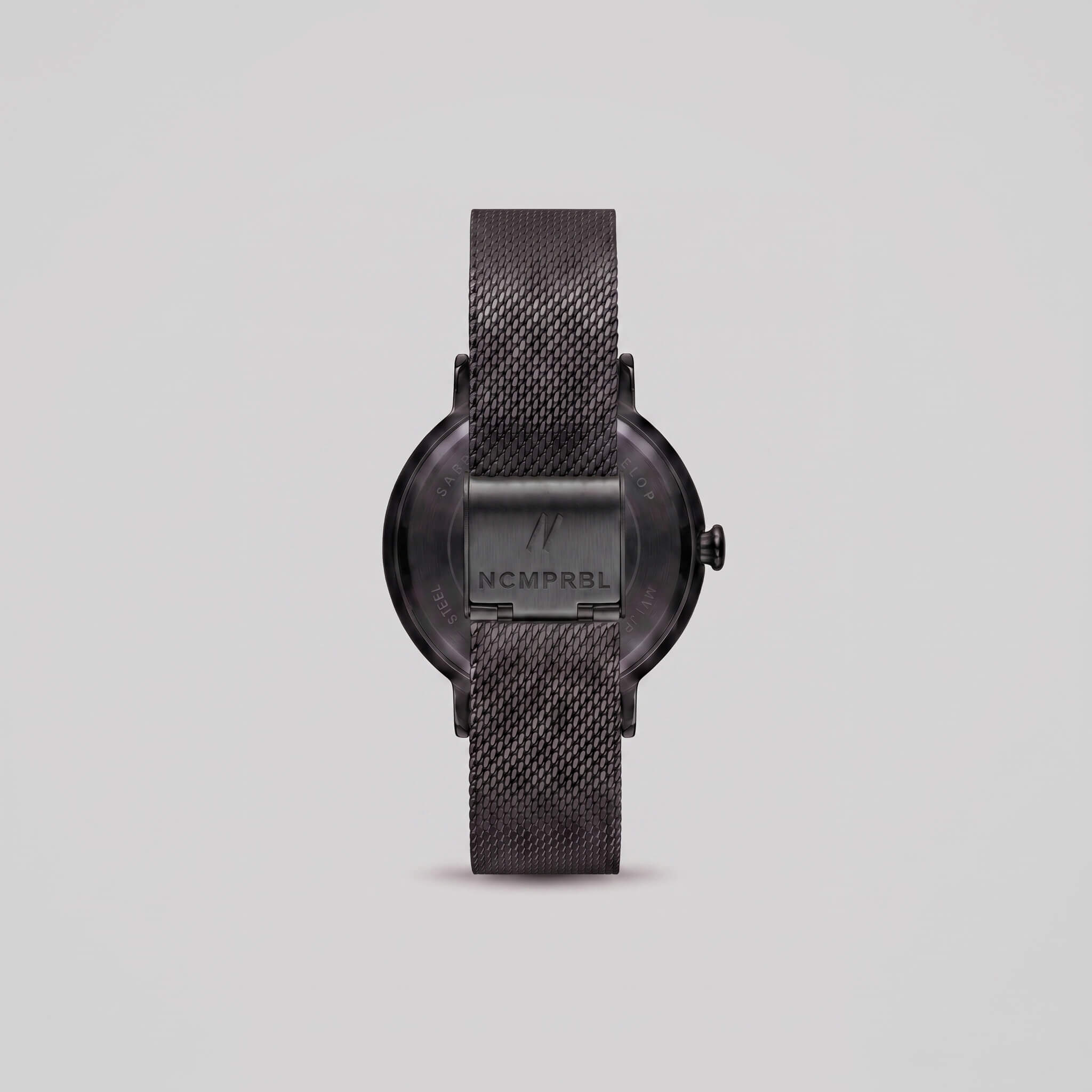 black  mesh strap watch shown from the back, featuring a round case with a visible 'NCMPRBL' brand logo on the center band, set against a solid light gray background.
