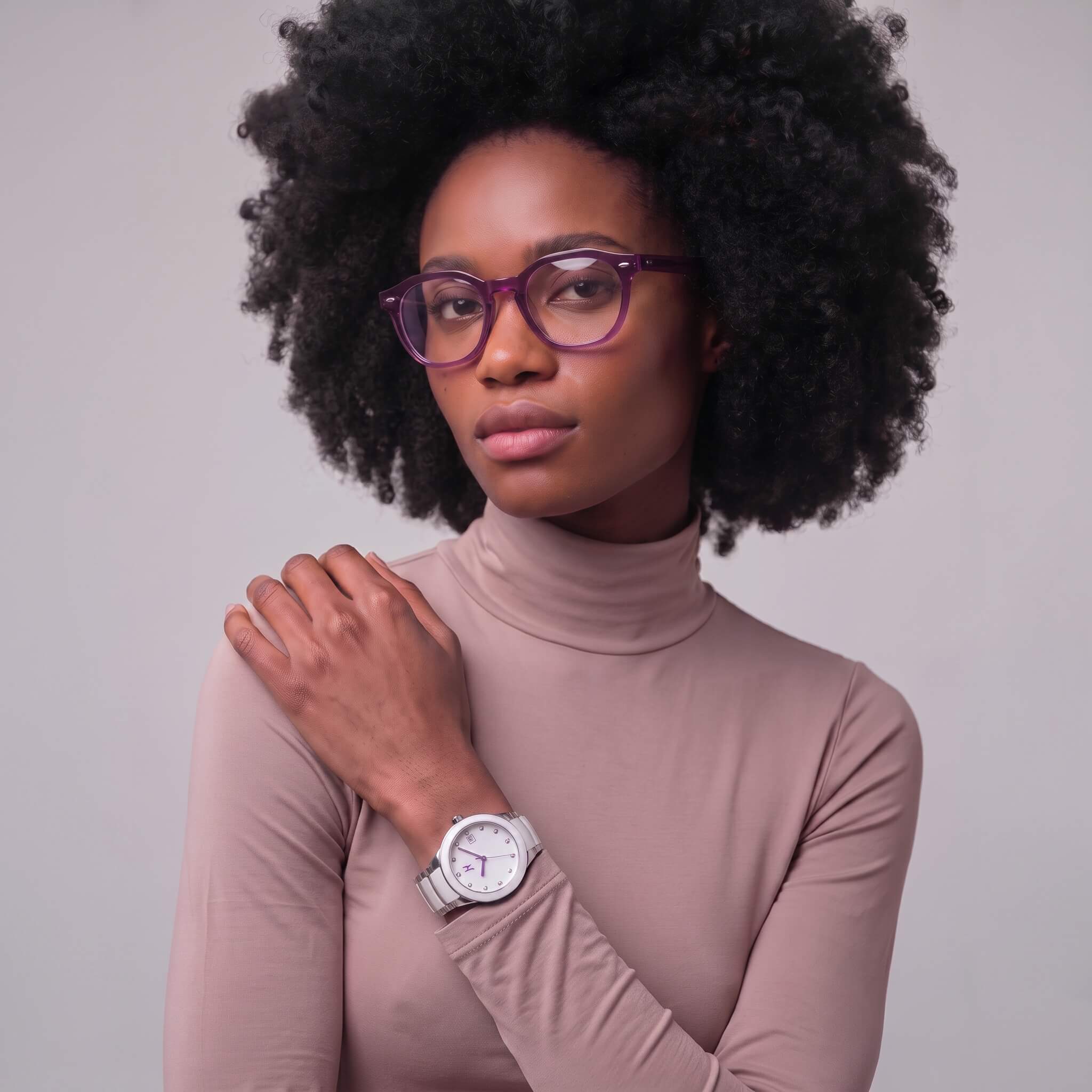 A woman with voluminous dark curly hair and haze 46mm geometric purple-framed eyeglasses, wearing a beige turtleneck top and a petite link purple reign silver watch with a white face, posed against a solid light gray background.
