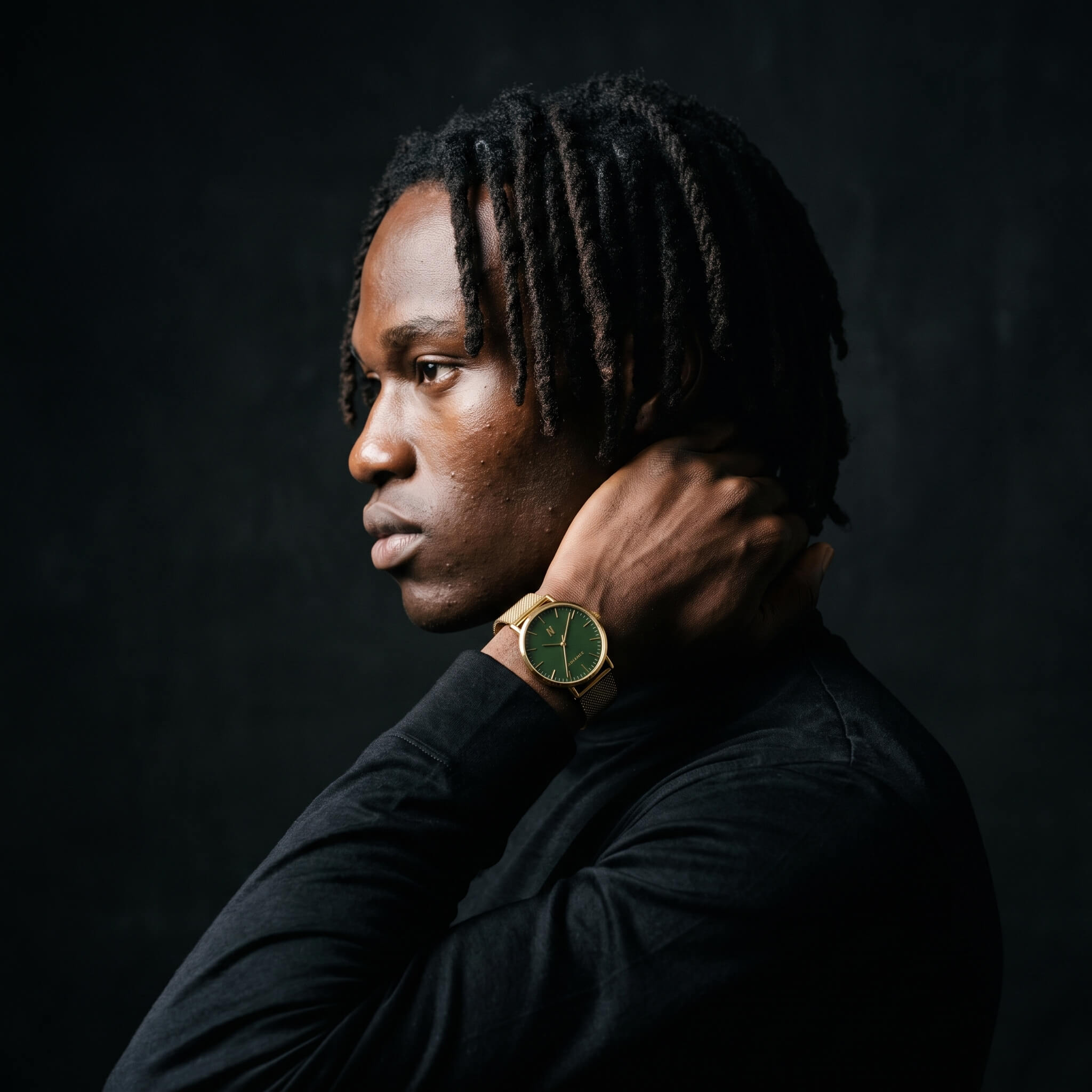 A man in a black long-sleeve shirt shown in profile against a dark studio background, wearing a advance mineral green 40mm mesh yellow gold wristwatch with a gold-tone case and a dark green dial.
